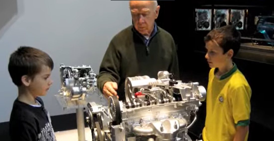 A grandfather teaching two boys at a cutaway engine display